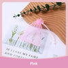 Pink organza drawstring jewelry gift bags with dried greenery displayed on a wooden surface.