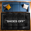 A dark gray doormat with the text SHOES OFF placed on a wooden floor.