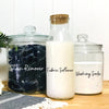 Three glass jars containing stain remover fabric softener and washing soda on a wooden surface