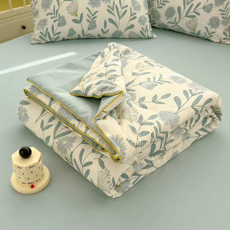 A light beige quilt with a blue floral pattern is displayed on a light blue surface next to a sewing gauge.