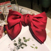 A vibrant red silk bow hair clip with a satin finish displayed on a white surface.
