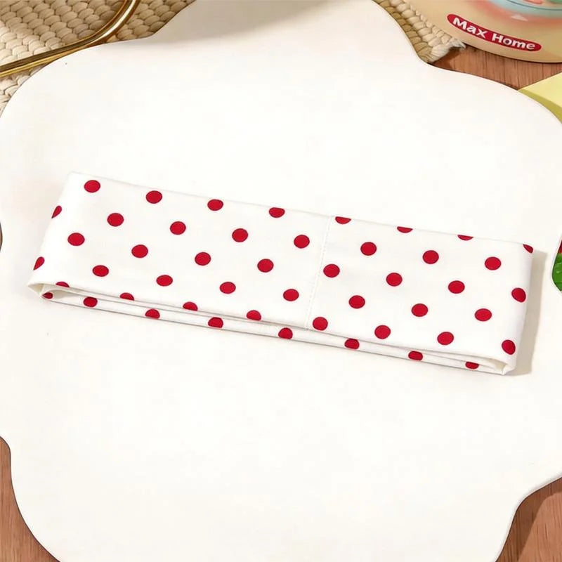 Un bandeau en tissu blanc à pois rouges est exposé sur une surface blanche.