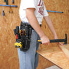 A person is holding a black heavy-duty tool pouch with a yellow belt clip and using it to clamp a piece of wood.