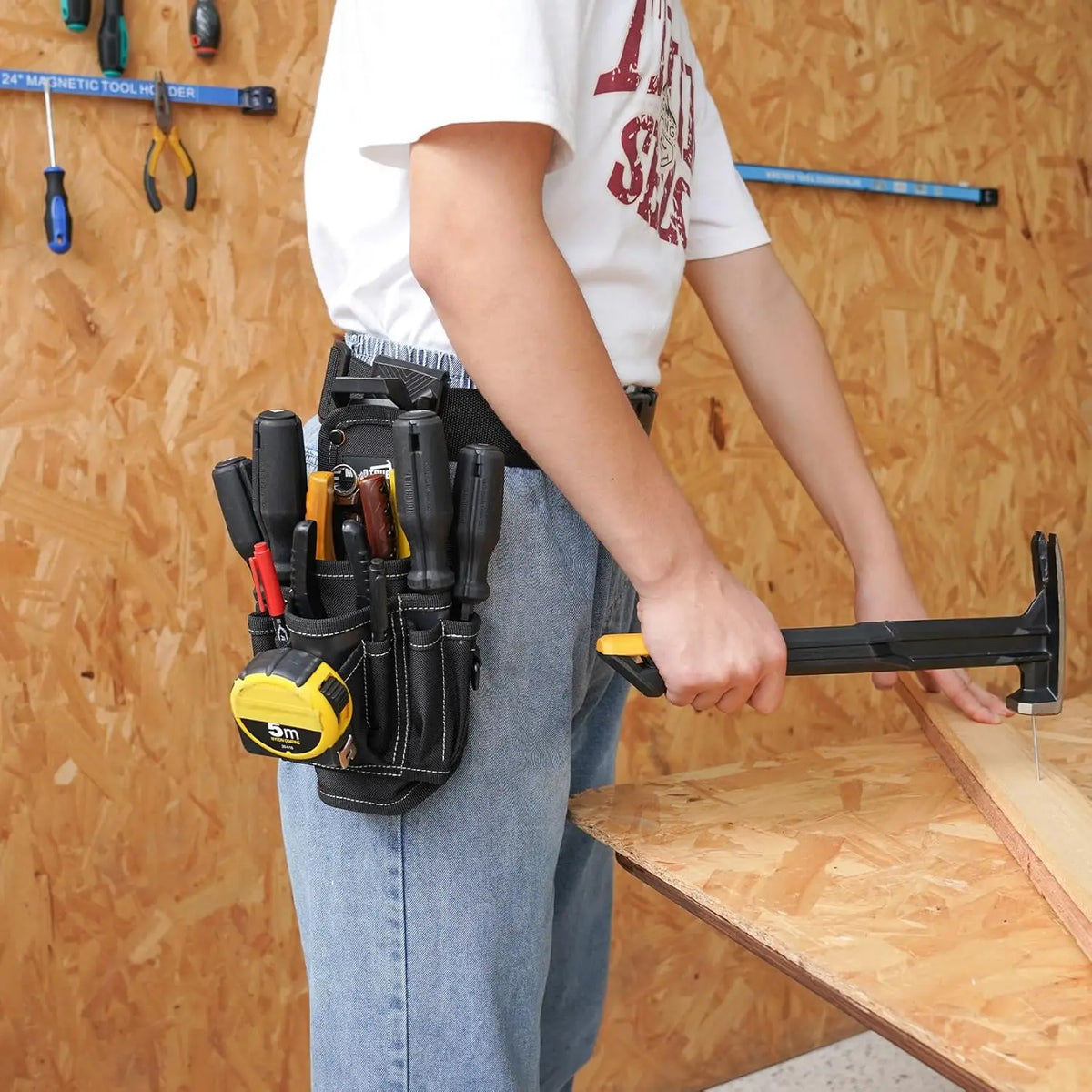 A person is holding a black heavy-duty tool pouch with a yellow belt clip and using it to clamp a piece of wood.