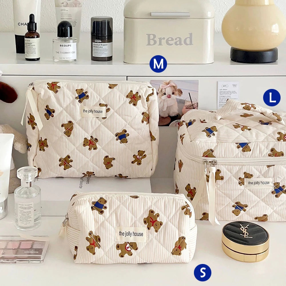 Eine Sammlung von beige- und weißen Bären-Make-up-Beuteln und einer brot-themed Storage Box werden auf einer weißen Oberfläch
