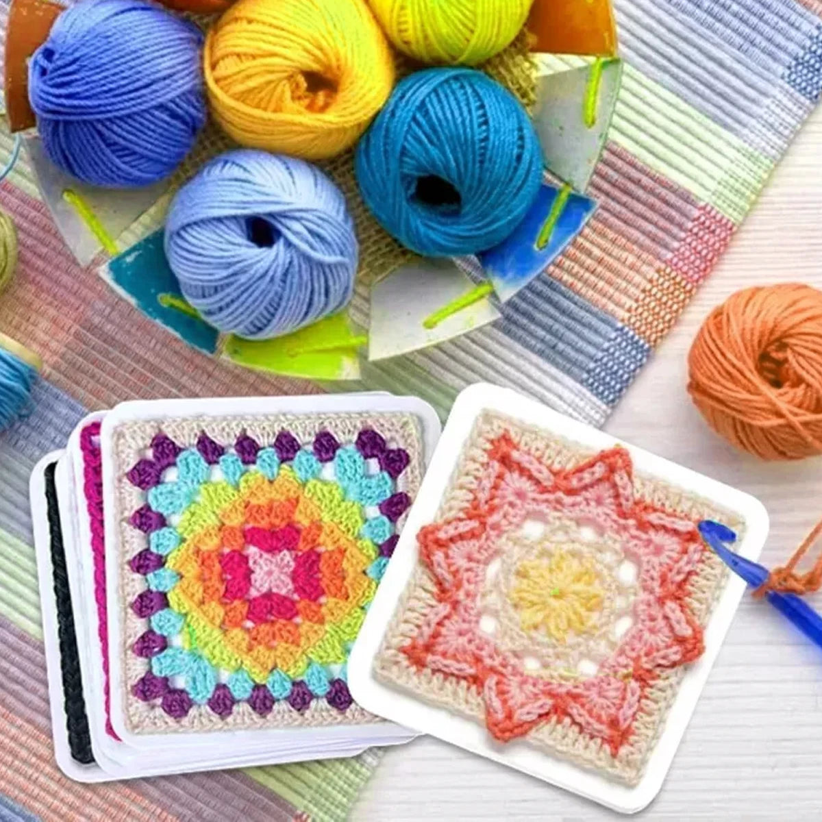 A collection of colorful crochet square pattern cards and yarn balls are displayed on a light surface.