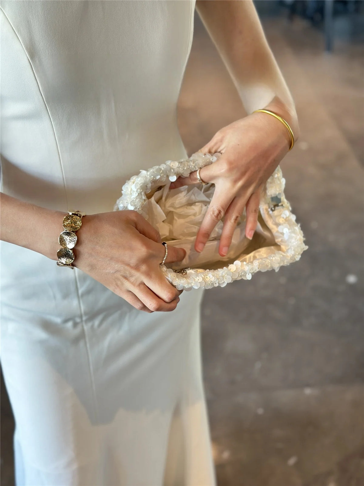 A person holds a white sequin beaded chain shoulder clutch bag in their hand.