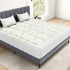 Matelas gris avec housse en viscose de bambou blanche à motifs de feuilles vertes sur un plancher en bois clair.