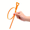 A hand holds an orange flexible drain cleaning tool with a curved wire end.