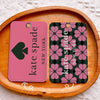 A pink card holder with a black spade design rests on a wooden board.