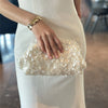A woman wearing a white dress holds a light gold sequin beaded chain shoulder clutch bag.