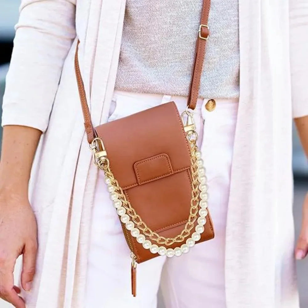 A brown leather purse with a pearl and gold chain is worn by a person in a light pink cardigan.