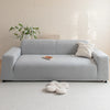 A light gray plush sofa cover with a white throw pillow and a small decorative item on a white carpet.