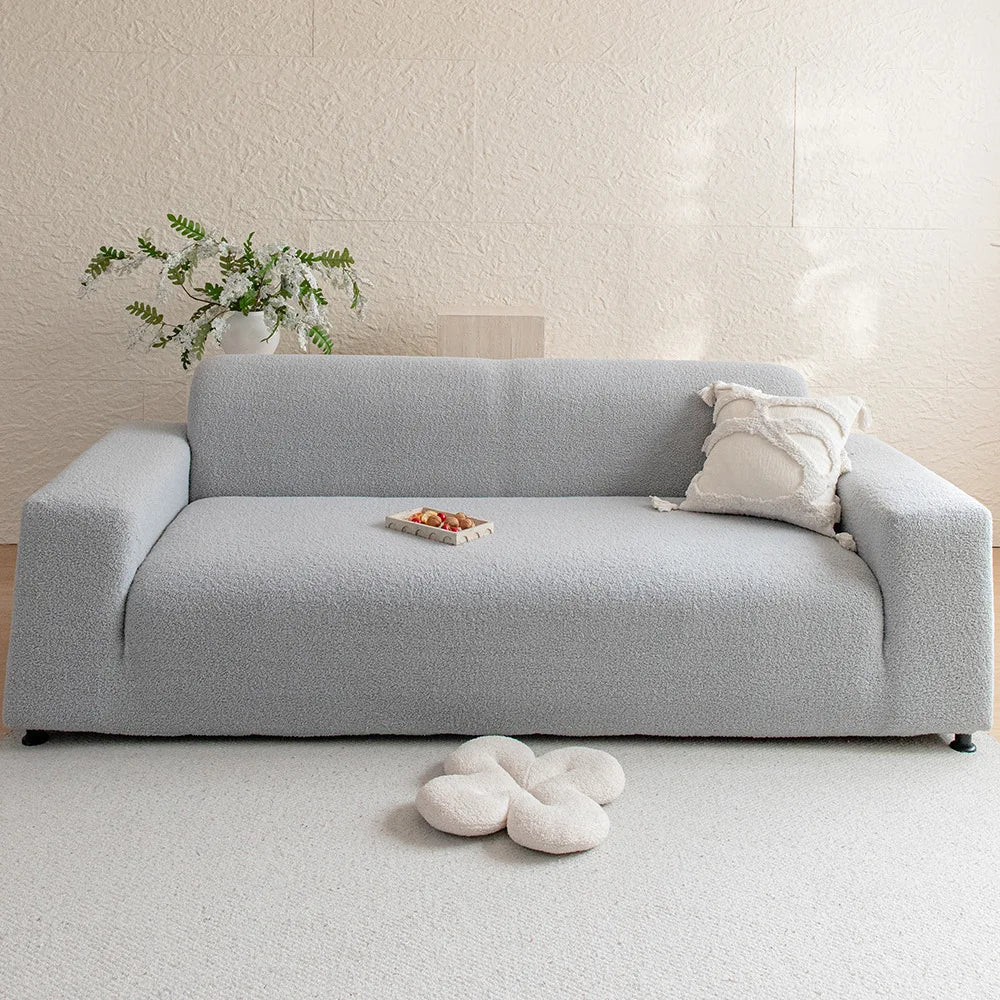 A light gray plush sofa cover with a white throw pillow and a small decorative item on a white carpet.
