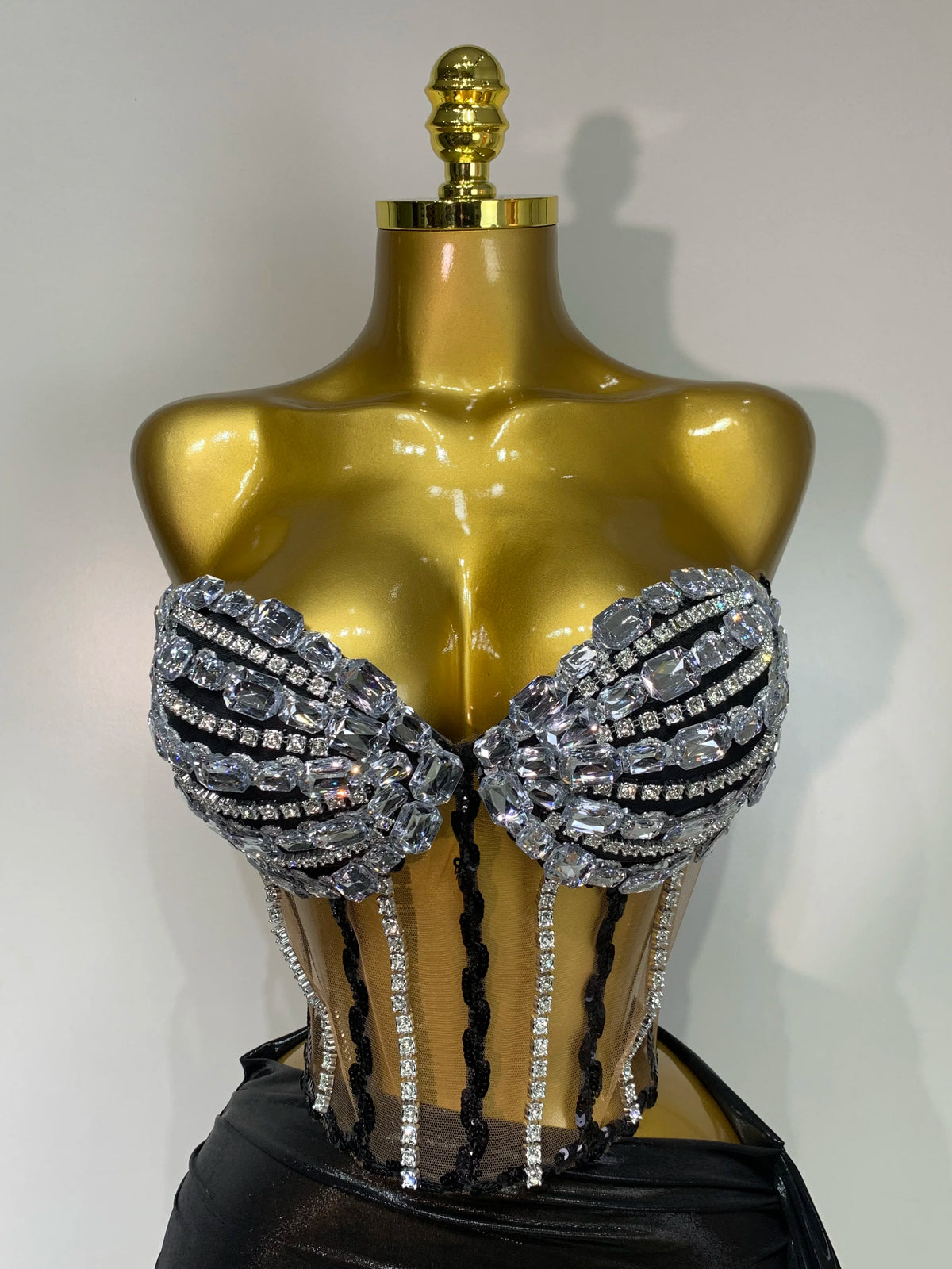 A gold-toned mannequin displays a sparkly two-piece party outfit with a see-through top and black accents.