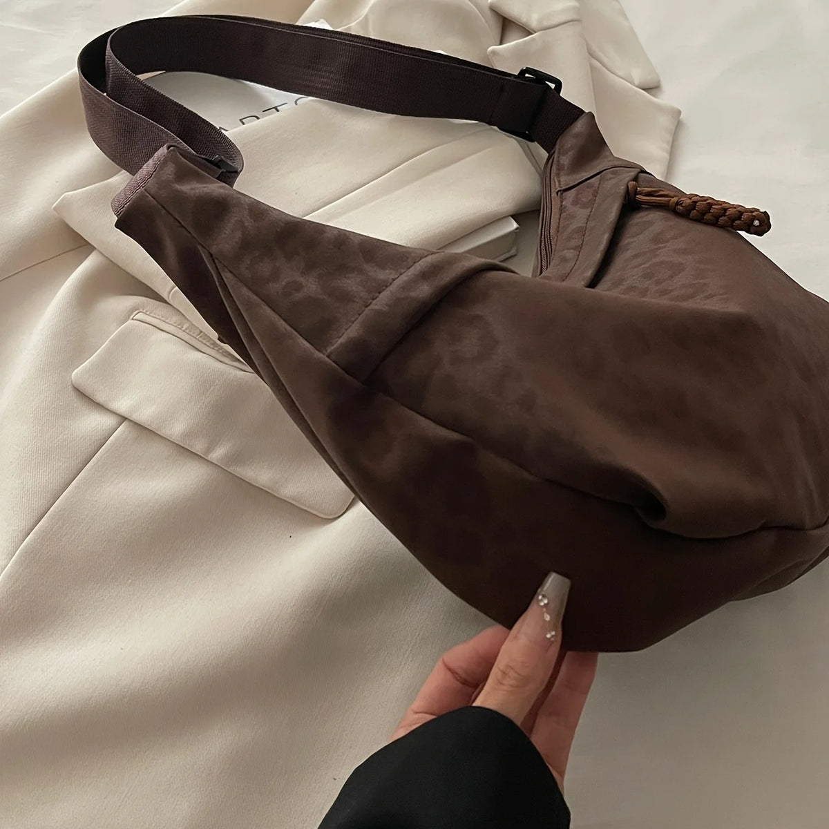 A dark brown leopard print crossbody bag is shown resting on a white blazer.
