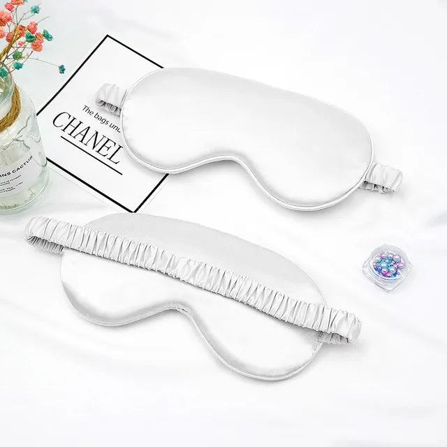 A white silk sleep mask with elastic straps is shown next to a box labeled CHANEL.