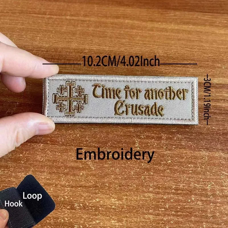 A rectangular beige embroidered patch with gold lettering that reads Time for another Crusade
