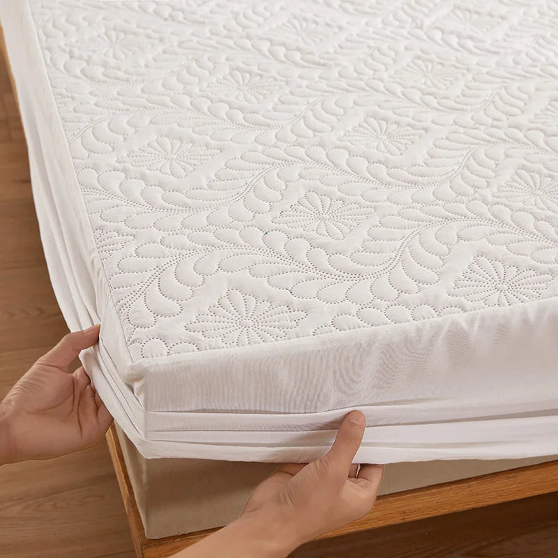 Hands are folding a white waterproof quilted mattress protector with extra padding on a wooden surface.