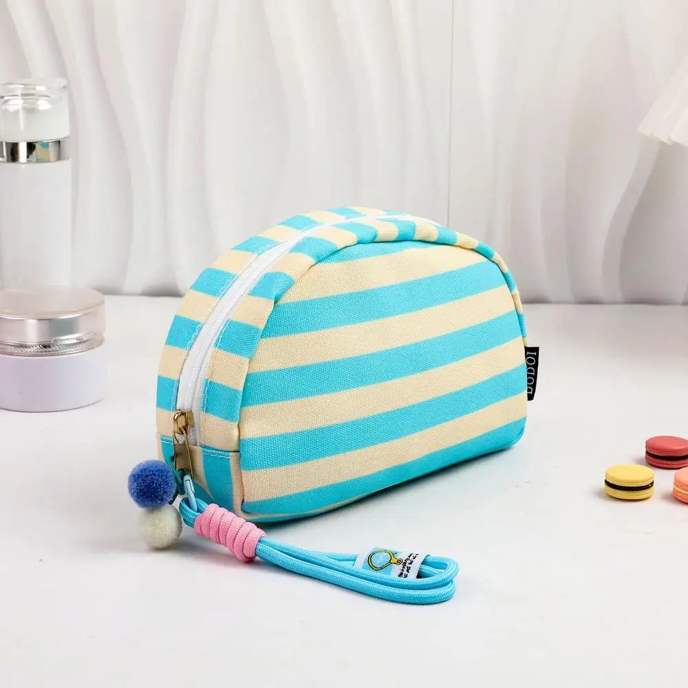 Pochette crochet rayée bleu clair et crème avec fermeture éclair et cordon rose, présentée sur une surface blanche.