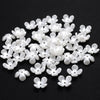 A pile of 100 white acrylic pearl spacer beads for jewelry making scattered on a black surface.