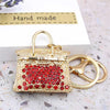 Gold handbag keychain decorated with red crystal rhinestones on a white background.