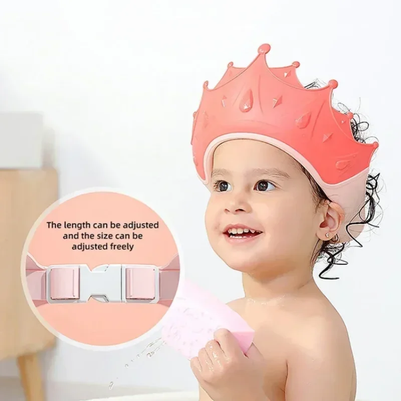 A baby is wearing a pink, adjustable shampoo shield cap with ear protection.