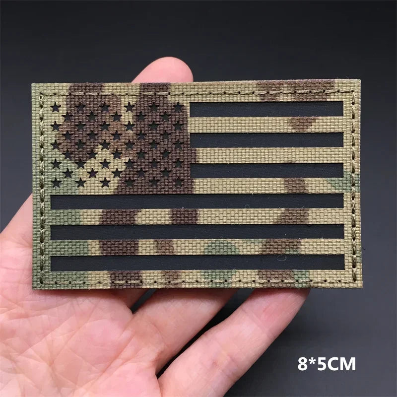 A rectangular tactical patch featuring a distressed American flag design in olive green and brown camouflage.