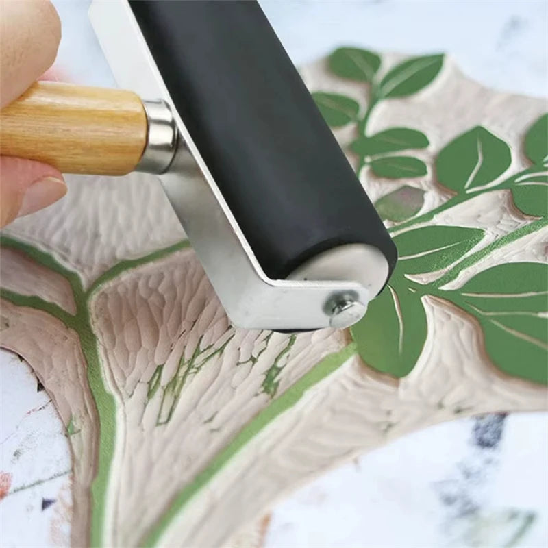 A close-up of a silver rubber ink roller set with a wooden handle resting on a light green leaf-shaped surface.