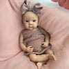 A newborn silicone reborn doll with a bow headband and a knitted outfit lying on pink fabric.