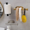 A stainless steel self-adhesive toilet paper holder with a white roll and a gold-toned towel bar displaying fluffy towels.
