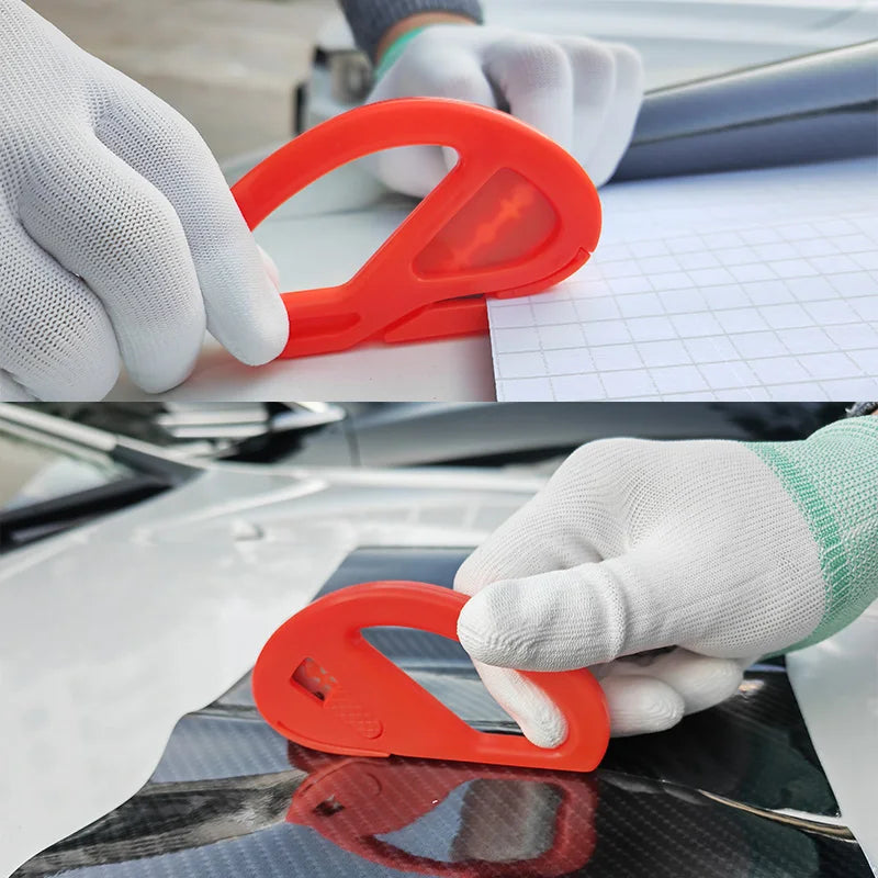 A hand wearing a white glove is using an orange vinyl wrap application tool on a surface.