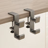 A close-up view of a modern, silver foldable aluminum desk hook mounted on a light wood surface.
