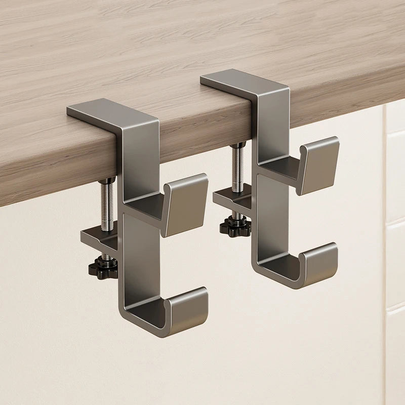 A close-up view of a modern, silver foldable aluminum desk hook mounted on a light wood surface.