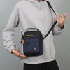 A person wearing a gray hoodie holds up a navy blue and black crossbody bag with an adjustable strap.
