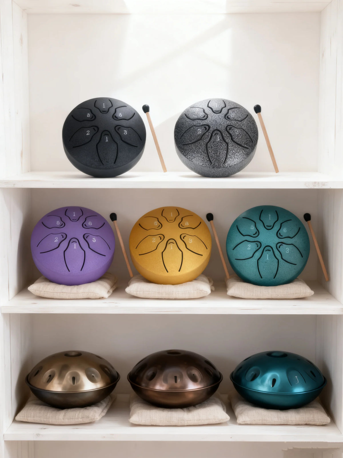 A collection of steel tongue drums in various colors including black, silver, purple, yellow, teal, and bronze displayed on w