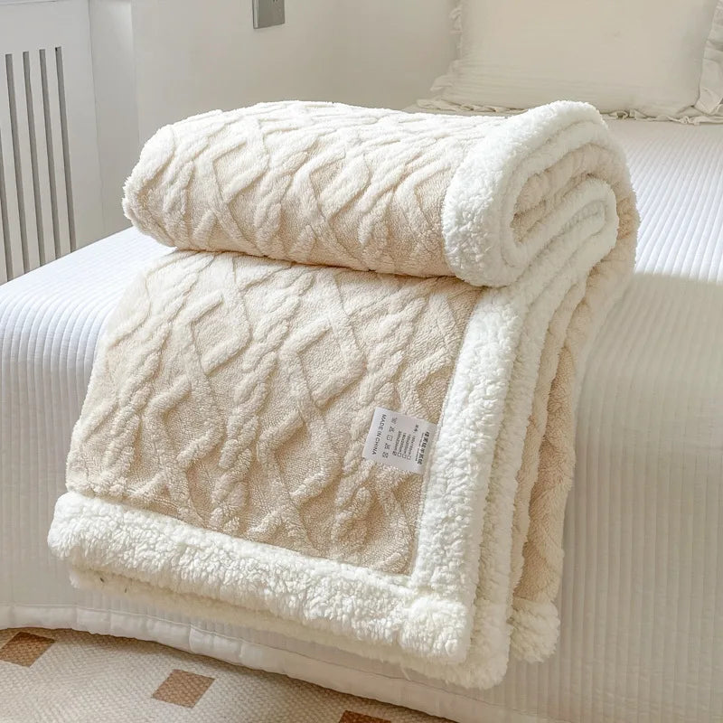 A cream colored double-layer fleece throw blanket folded on a white bed with a white duvet.