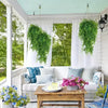 Artificial green hanging vine greenery decorating a porch with white curtains and outdoor furniture