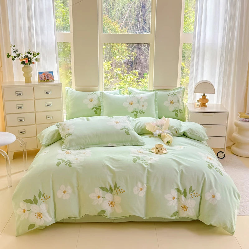 A light green printed duvet cover set with matching pillowcases displayed on a bed near a large window.
