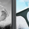A hand is using a green window cleaning brush to wipe a glass window pane.