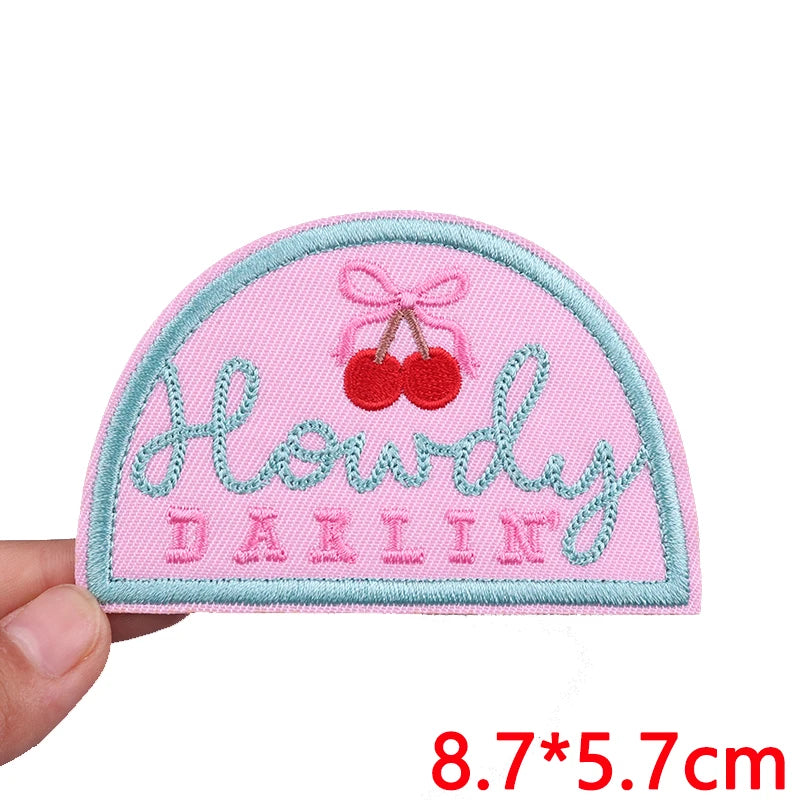 Pink embroidered patch with the text Howdy Darling in light blue thread and a red cherry design
