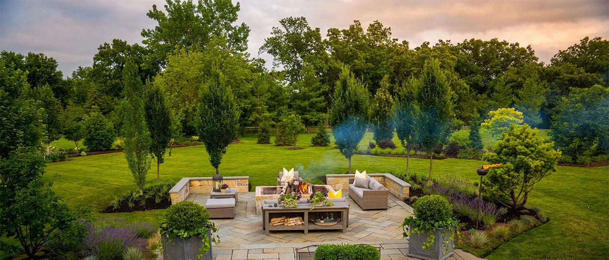 Weatherproof patio furniture cover shown on a wooden deck surrounded by lush greenery and trees.