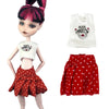 A fashion doll wearing a red polka dot skirt and a white t-shirt with rock angel embroidery.