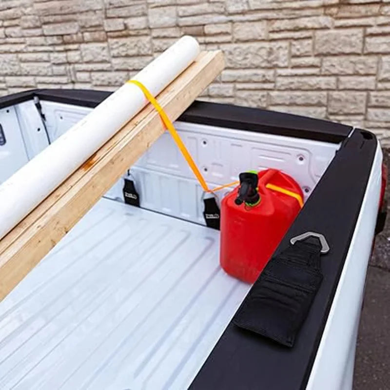 A white foam rod is tied to a wooden plank and placed inside a black truck tailgate, next to a red bottle and a black strap.