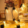 A close-up of vintage Edison bulbs strung on black wires, illuminating a white vase and warm light.