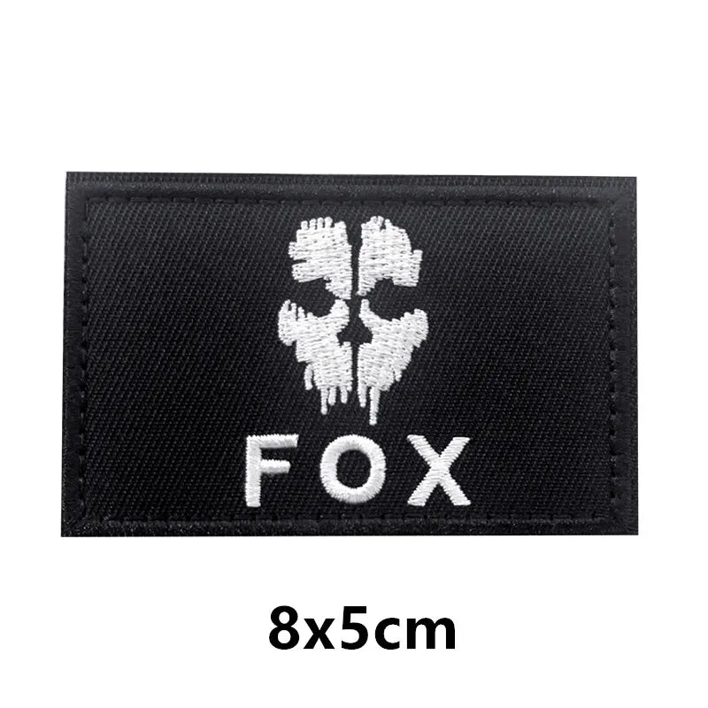 Black embroidered patch featuring a white fox head design and the text FOX on a fabric backing.