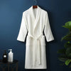 A white waffle knit robe hanging on a dark blue wall next to a potted green plant.