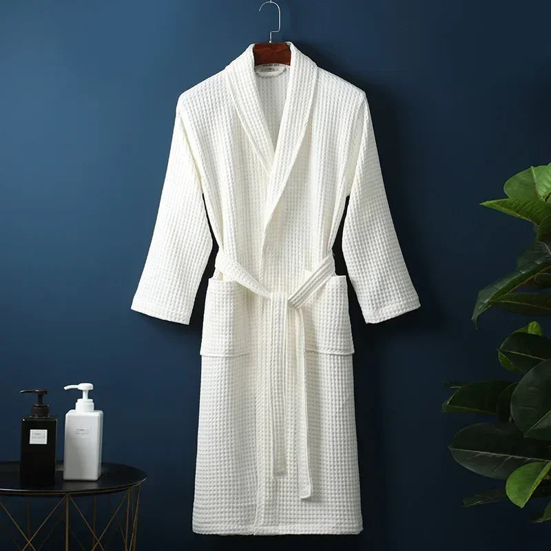 A white waffle knit robe hanging on a dark blue wall next to a potted green plant.