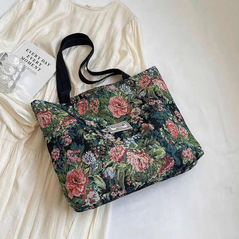 A dark floral print corduroy tote bag with pink and green accents resting on a white fabric background.