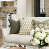 A white sofa decorated with various floral patterned throw pillows and a vase of white roses in a bright interior.